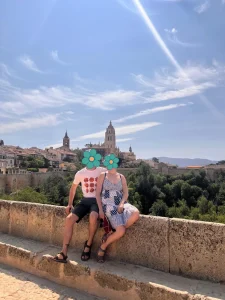Mi pareja y yo sentados en un mirador con vistas a la Catedral de Segovia, bajo un cielo azul y rodeados de naturaleza.