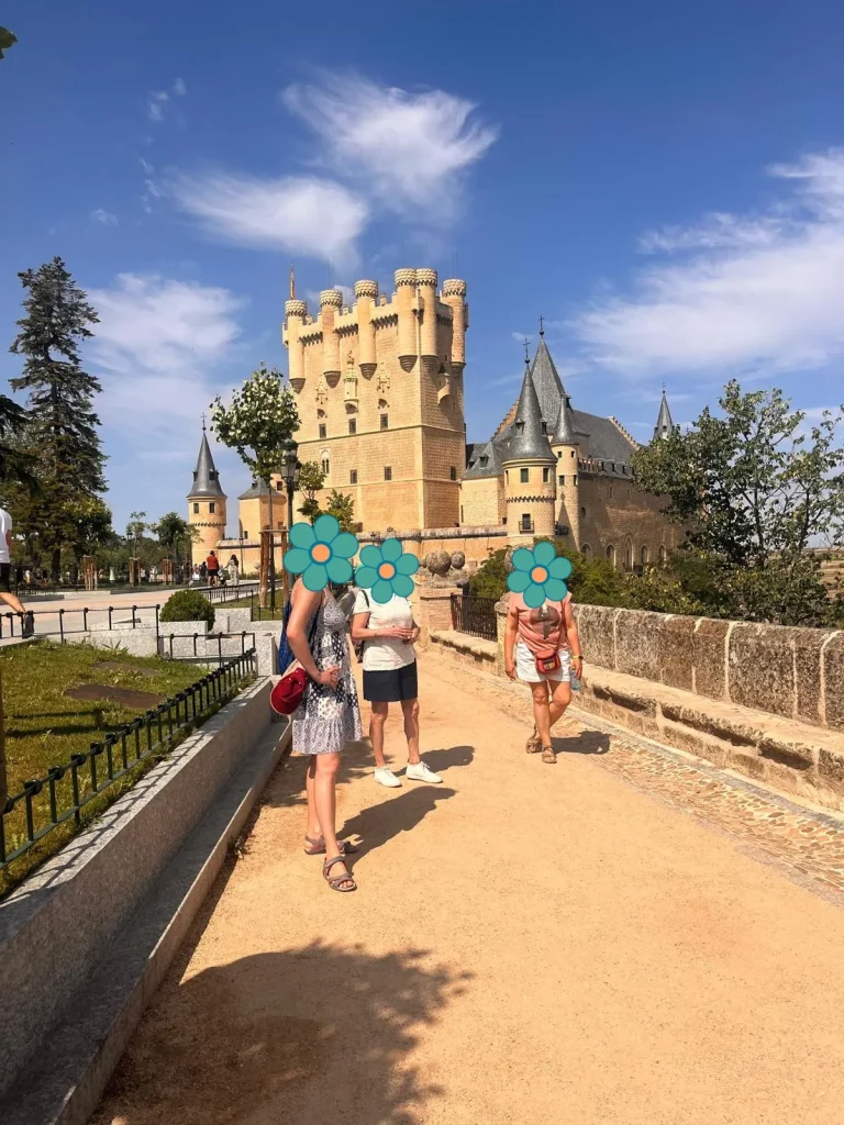 Paseo en familia cerca del Alcázar de Segovia, con su arquitectura de cuento de hadas al fondo y un cielo azul con nubes suaves.
